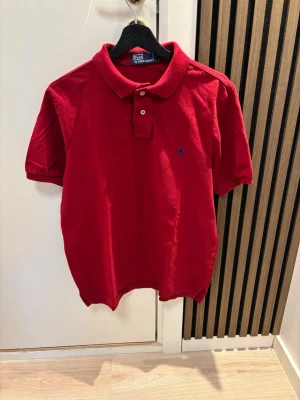 Röd pikétröja från Polo Ralph Lauren - Klassisk röd pikétröja från Polo Ralph Lauren med korta ärmar och blå broderad logga på bröstet. Tröjan har krage, två knappar framtill och är gjord i mjuk bomull. Perfekt till en avslappnad men ändå stilren look. Kom dm för eventuella frågor 🧐pris kan diskuteras 💯😇