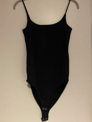 Svart body med smala axelband Stradivarius - Säljer en enkel och stilren svart body från Stradivarius i storlek XS. Bodyn har smala axelband och knäppning med tryckknappar nedtill. Perfekt att styla till jeans eller kjol för en clean look.