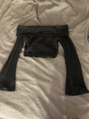 Grå ribbad offshoulder topp - Säljer en grå ribbad offshoulder topp med långa ärmar. Toppen är croppad och har en bred kant upptill som ger en snygg siluett. Perfekt för dig som gillar trendiga och stilrena plagg med en twist.