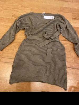  stickad klänning med knyt - Snygg stickad klänning med knytband i midjan. Klänningen har lång ärm och rund. Enkel att styla 