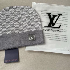 Grå rutig mössa - Säljer en snygg grå mössa med klassiskt rutigt mönster och logga framtill. Mössan har en bred uppvikt kant och är perfekt för dig som vill ha en stilren accessoar med lyxig känsla.