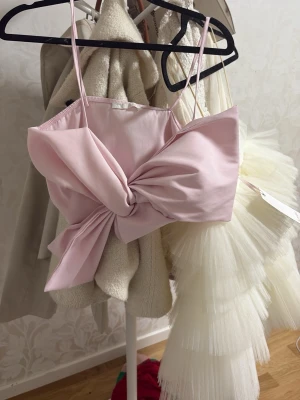 Ljusrosa bandeau topp med stor rosett - Supersöt ljusrosa bandeau topp med tunna axelband och en stor, iögonfallande rosett framtill. Toppen är croppad. Perfekt till sommaren, aldrig använd 