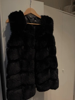  pälsväst - Säljer en svart pälsväst från garoff med breda, horisontella paneler och mjuk, fluffig känsla. Västen är ärmlös och har en stilren look utan synliga knappar eller dragkedja. Perfekt för att lyfta vilken outfit som helst under kyligare dagar. Har även fickor. Storlek 36. Pris kan diskuteras!