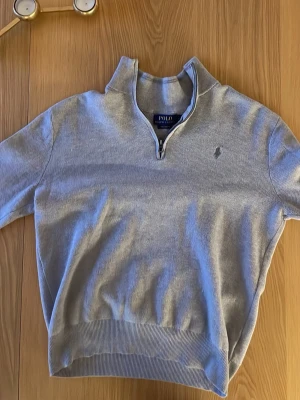 Grå half zip tröja Polo Ralph Lauren - Säljer en stilren grå tröja från Polo Ralph Lauren i mjuk pima bomull. Tröjan har half zip-dragkedja, ribbade muddar och diskret logga på bröstet. Perfekt till lager på lager och funkar året runt.