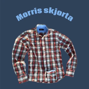 Rutig skjorta från Morris i bomull - Säljer en klassisk rutig skjorta från Morris i bomull. Skjortan har röda, gröna, blå och vita rutor, knappar framtill och lång ärm. Insidan av kragen är ljusblå och bröstet har Morris-loggan broderad. Perfekt för dig som gillar preppy stil.