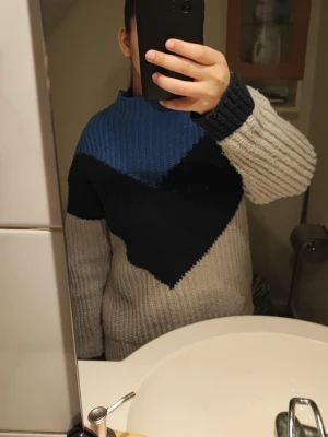 Stickad tröja med blå och marinblå detalj - Säljer en chunky stickad tröja. Tröjan har hög halg och den har en cool färgblock-design. Väldigt tjock och varm. Använd och har några prickar. Storlek S 