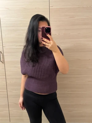 Mörklila stickad topp - Säljer en chunky stickad tröja i mörklila med korta ärmar och bred ribbad midja. Tröjan har en loose fit upptill och sitter tajtare vid midjan, perfekt för lager på lager under höst och vinter. Supermjuk och skön att bära.