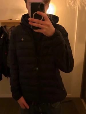 Marinblå pufferjacka från Morris, M - Säljer en Marinblå pufferjacka från Morris i storlek medium. Jackan har quiltad design, dragkedja framtill och en liten logga på bröstet. Materialet är syntet och jackan har långärmade ärmar. Bara att höra av er vid frågor eller bud!😊