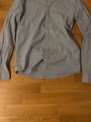 Ljusblå skjorta från Tommy Hilfiger - Klassisk ljusblå skjorta från Tommy Hilfiger med diskret logga broderad på bröstet. Skjortan har lång ärm, knappar framtill och är tillverkad i mjuk bomull. Perfekt till jeans eller chinos för en clean och stilren look.