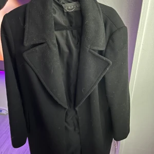 Svart lång kappa från Esprit - Säljer en svart lång kappa från Esprit med klassisk krage och enkel, stilren design. Jackan har långa ärmar och är tillverkad i ett mjukt ullmaterial. Perfekt för dig som vill ha en tidlös och snygg look under kyliga dagar.