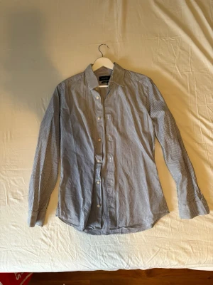 Randig blåvit skjorta från Riley - Snygg blåvit randig skjorta från Riley i super slim fit. Skjortan har klassisk krage, långa ärmar och knappar framtill. Perfekt för dig som gillar en smalare passform och stilren look.