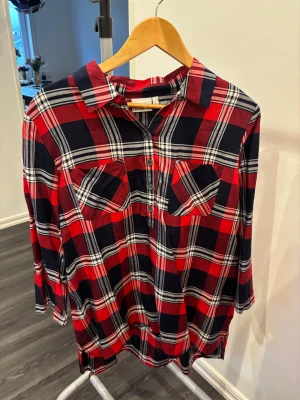 Rutig röd och marinblå skjorta Isolde - Rutig skjorta från Isolde i rött, marinblått och vitt. Skjortan har klassisk krage, knappar framtill och två bröstfickor. Tillverkad i mjuk bomull och har långa ärmar. Perfekt för en avslappnad och cool look.