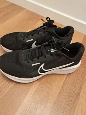 Nike löparskor (41) - Nike löparskor i svart mesh med vit-svart sula och stor vit swoosh på sidan. Skorna har snörning och en platt sula som ger bra grepp. Lätt och ventilerande material, perfekt för dig som gillar att springa eller träna. Snygg och sportig design med diskreta detaljer. Nypris 799kr. Säljer för 330kr. (Använda ca 5 gånger).
