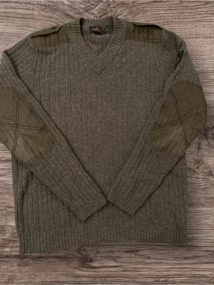 Grå stickad tröja från Morris - Snygg grå stickad tröja från Morris med ribbad struktur, v-ringad hals och coola quiltade detaljer på axlar och armbågar. Långärmad med broderad patch på ena ärmen som ger en schysst touch. Perfekt för dig som gillar klassisk stil med lite edge.