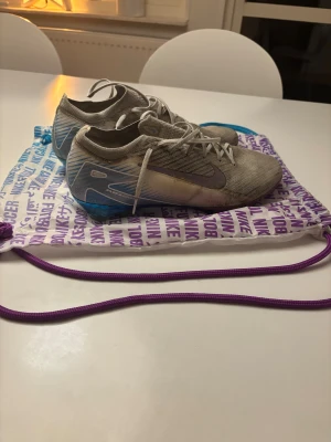 Nike Mercurial fotbollsskor blå/lila - Nike Mercurial fotbollsskor i vit, lila och blå. Skorna har snörning och en platt sula med dobbar för gräsplan. Ovandelen är i syntetmaterial med mönstrade linjer och Nike-logga på sidan. Snygg, sportig design som sticker ut på planen. Dessa skor är limited edition och går ej att få tag på nya längre. Nypris 3500kr!
