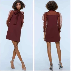 Vinröd kortklänning med rosett från Zara - Vinröd kortklänning från Zara med transparenta långärmar och stor knytrosett i halsen. Klänningen har en lätt A-linjeform och är gjord i ett tunt, syntetiskt material som ger en luftig känsla. 