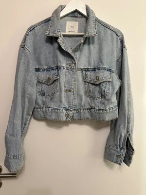 Ljusblå croppad jeansjacka från mango stl m  - Säljer en ljusblå croppad jeansjacka från mango i stl m med klassisk krage, två bröstfickor och knappar framtill. Jackan har långa ärmar och en avslappnad passform. Jackan är använd men i god skick 
