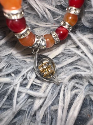  lace_ orange_yellow_red_crown - Unikt halsband med pärlor i rött och orange, dekorerade med silvriga detaljer. Hängsmycket har en cool design med silver och guldtoner samt glittrande stenar. Perfekt accessoar för dig som gillar färg och bling. Namn  ”lace_ orange_yellow_red_crown” artikelnummer ”09WQ” 