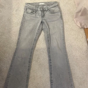 Grå bootcut jeans från Gina Tricot - Snygga grå jeans från Gina Tricot med bootcut passform och markerade sömmar. Modellen har låg midja, klassiska fem fickor och bakfickor med lock och silverfärgade knappar. Perfekt till vardagen!