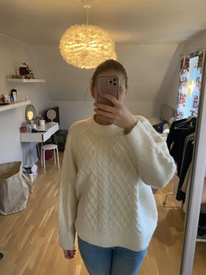 Vit stickad tröja från Lager 157, storlek M - Mysig vit stickad tröja från Lager 157 i storlek M. Tröjan har ett snyggt flätmönster framtill, ribbade muddar och rund hals. Perfekt för kalla dagar och passar till jeans eller kjol. Materialet är mjukt och värmande, med långärmad passform och loose fit.