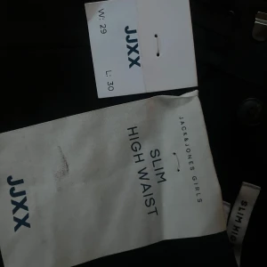 Svarta slim high waist byxor JXX - Svarta byxor från JXX med slim fit och hög midja. Snygg, stilren look med raka ben och diskret dragkedja i sidan. Perfekta för dig som gillar en tajtare passform och vill ha en klassisk svart byxa i garderoben.