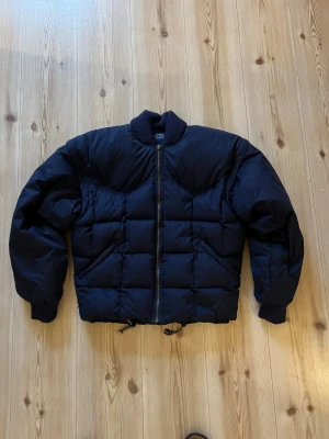 Mörkblå dunjacka/väst från Boomerang S - Säljer en mörkblå dunjacka från Boomerang i storlek S. Jackan är quiltad med boxig passform, ribbade muddar och dragkedja framtill. Yttermaterialet är polyester och fodret består av 90% dun och 10% fjäder. Klassisk broderad logga på ärmen. Dragkedja vid årmarna så man kan göra en väst.