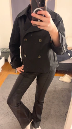 Svart skepparkavaj från Esmara - Säljer en svart skepparkavaj från Esmara i storlek 40. Jackan har dubbelknäppning med stora knappar, klassisk krage och raka fickor framtill. Materialet är slätt och känns som polyester. Ärmarna har snygga knappdetaljer vid mudden. Perfekt för dig som gillar stilrena och tidlösa plagg.