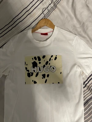 HUGO T-shirt  - Snygg vit t-shirt från HUGO i bomull med ett stort tryck på bröstet i beige. Tröjan är i storlek M, med inga skador alls 