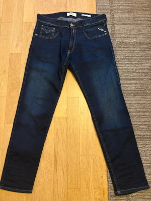 Mörkblå Replay jeans - Snygga mörkblå jeans från Replay med klassisk femficksdesign och kontrastsömmar. Modellen har raka ben och normal passform, midwaist och diskret Replay-logga på bakfickan. Materialet är stretchigt jeans med inslag av elastan för extra komfort.