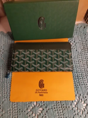 Grön Goyard plånbok med mönster - Snygg grön plånbok från Goyard med klassiskt grafiskt mönster och silverfärgad dragkedja. Plånboken har flera fack inuti och detaljer i skinn. Perfekt för dig som vill ha något unikt och lyxigt i väskan.