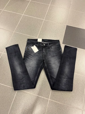 Svarta slimmade jeans från tiger of sweden W29 L34 - Snygga svarta jeans från Tiger of sweden i tvättad look. Modellen har tight passform med smala ben och klassiska fem fickor. Jeansen har knapp och dragkedja framtill samt bälteshällor. Perfekta för dig som gillar en smal siluett.