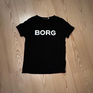 Svart Björn Borg t-shirt med tryck - Svart t-shirt från Björn Borg med stort vitt BORG-tryck på bröstet. Klassisk rund hals och korta ärmar. Tillverkad i mjuk bomull som känns skön mot huden. Perfekt för dig som gillar enkel och stilren design.