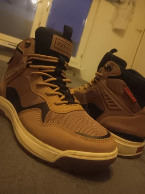 Venice Originals bruna high-top sneakers - Snygga high-top sneakers från Venice Originals i brun och svart med beige sula. Skorna har snörning, robust platt sula med hexagonmönster och detaljer i syntet och mesh. Perfekt för dig som gillar streetwear och vill ha en cool look.