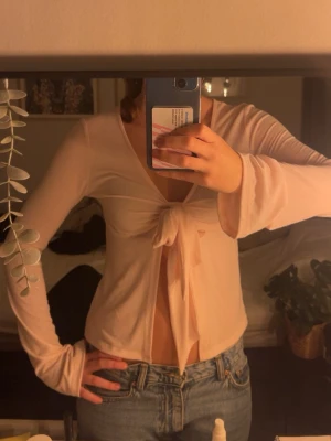 Ljusrosa omlottopp med knyt - Säljer en ljusrosa omlottopp med långa ärmar och snygg knytning framtill. Toppen har v-ringad hals och är croppad, vilket ger en trendig look. Perfekt att styla med jeans eller kjol för en cool vibe. Oanvänd❤️