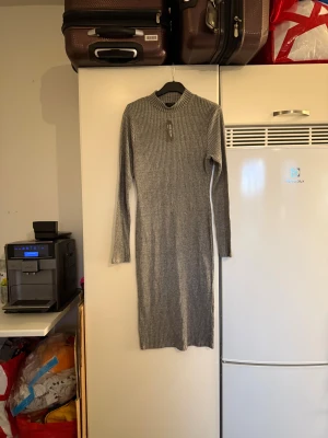Grå ribbad långklänning River Island - Snygg grå ribbad långklänning från River Island med lång ärm och hög krage. Klänningen har en tight passform och är tillverkad i ett stickat material som ger en skön känsla. Perfekt för dig som gillar stilrena och enkla plagg med en modern touch. Storlek 40. Kanske passar en M/L. Helt ny med tags/ prislapp fortfarande kvar. 