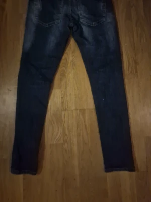 Mörkblå skinny jeans med slitningar - Säljer ett par mörkblå skinny jeans med slitningar och tvättade detaljer. Jeansen har klassisk femficksmodell och smal passform. Perfekta för dig som gillar en trendig och avslappnad stil.