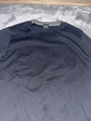 Svart sweatshirt från Hugo Boss - Snygg svart sweatshirt från Hugo Boss med diskret präglad logga på bröstet. Tröjan har rund halsringning, långa ärmar och slim fit-passform. Perfekt för en stilren och modern look.