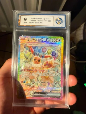 Pokémon Eevee ex Alt Art Terastal - Japanskt Pokémonkort Eevee ex Alt Art från 2024 Terastal Festival sv8a 223, graderat Mint 9 av RaukCard. Kortet har en färgglad holografisk design med Eevee och kristallmotiv. Perfekt för samlare som gillar exklusiva och ovanliga Pokémonkort.