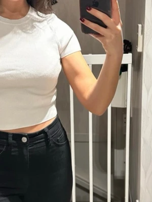 Vit croppad topp från Zara - Säljer en enkel och stilren vit croppad topp från Zara. Toppen har rund halsringning, korta ärmar och är ribbad i materialet vilket ger en snygg struktur. Perfekt till jeans eller kjol för en clean look. Står storlek M men mer S/XS.