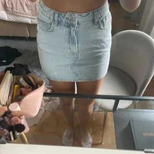 Ljusblå jeanskjol med fickor - Trendig ljusblå jeanskjol i kort modell med klassiska fickor både fram och bak. Kjolen har knapp- och dragkedjestängning framtill och är perfekt för en avslappnad och cool stil. Passar till allt från sneakers till boots.