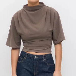 croppad topp med hög hals - Säljer en brun croppad topp med hög hals och korta, vida ärmar. Toppen har snygg rynkdetalj i sidorna som ger en tight passform över midjan. Perfekt till jeans eller kostymbyxor för en stilren look. Nypris 300kr