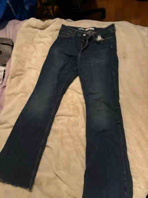 Levi's 517 blå bootcut jeans - Säljer ett par klassiska blå ming jeans med bootcut passform. Jeansen har fem fickor, normal midja och råa kanter längst ner på benen för en avslappnad look. Perfekta för dig som gillar vintagevibbar och tidlös denimstil.