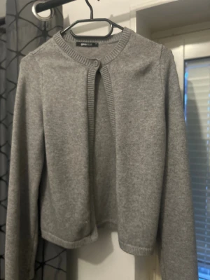 Grå kort kofta från Gina Tricot Org pris 356kr - Snygg grå kofta från Gina Tricot i kort modell med rund halsringning och en knapp framtill. Tillverkad i mjukt stickat material och har ribbade kanter vid hals, ärmslut och nederkant. Perfekt att slänga över en topp för en enkel look.