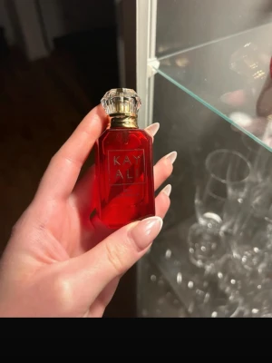 Kayali JUICY Apple parfym    - Snygg parfym från Kayali i en lyxig röd glasflaska med gulddetaljer och en kristalliknande kork. Flaskan har en elegant, geometrisk form och texten 'KAYALI' i guld på framsidan. Perfekt för dig som gillar exklusiva dofter och snygg design.