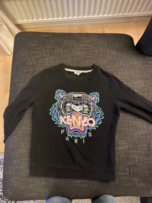 Svart sweatshirt med tiger från Kenzo - Svart sweatshirt från Kenzo med ikoniskt broderat tigerhuvud i flera färger och texten 'KENZO PARIS' framtill. Storlek xs men passar till s också nästan helt oanvänd jätte bra skick