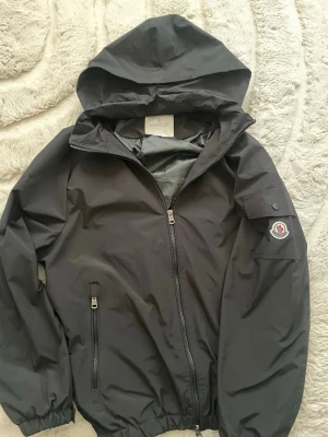 Svart vindjacka från Moncler - Snygg svart vindjacka från Moncler med huva och dragkedja framtill.  Jackan är riktigt feeeetttt 