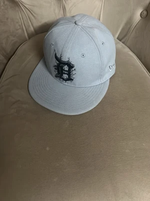 Grå New Era 59FIFTY keps MLB - Säljer en stilren grå New Era 59FIFTY keps med svart broderad MLB-logga framtill och klassisk MLB-märke bak. Kepsen är i 100% polyester och har en grön undersida på skärmen. Perfekt för dig som gillar streetwear och sportig stil. Sparsamt använd, äkta