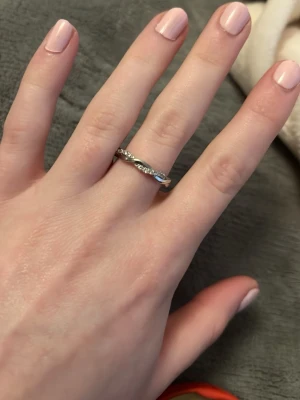 Silverfärgad ring med stenar - Säljer en stilren silverfärgad ring med gnistrande stenar runt hela bandet. Ringen har en tunn och elegant design som passar perfekt för dig som gillar diskreta men snygga accessoarer. Perfekt att bära ensam eller att kombinera med andra ringar.Vid köp av fler ringar kan jag slå ihop annonserna så frakten blir billigare.