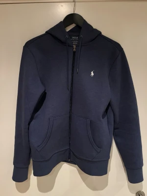 Polo Ralph Lauren Zip hoodie - Mörkblå hoodie med dragkedja från Polo Ralph Lauren. Bara använd max 4 gånger då den inte passar mig. Skicket är som helt nytt. Bara att höra av sig vid funderingar. 