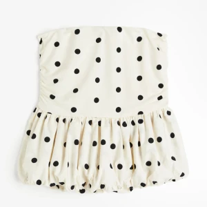 H&M Prickig tubtopp med volang - Från H&M. Trendig axelbandslös tubtopp i vit med svarta prickar och volang nedtill. Toppen har en ballongliknande form och är perfekt för dig som vill sticka ut. Passar till både jeans och kjol för en trendig look. XS-S